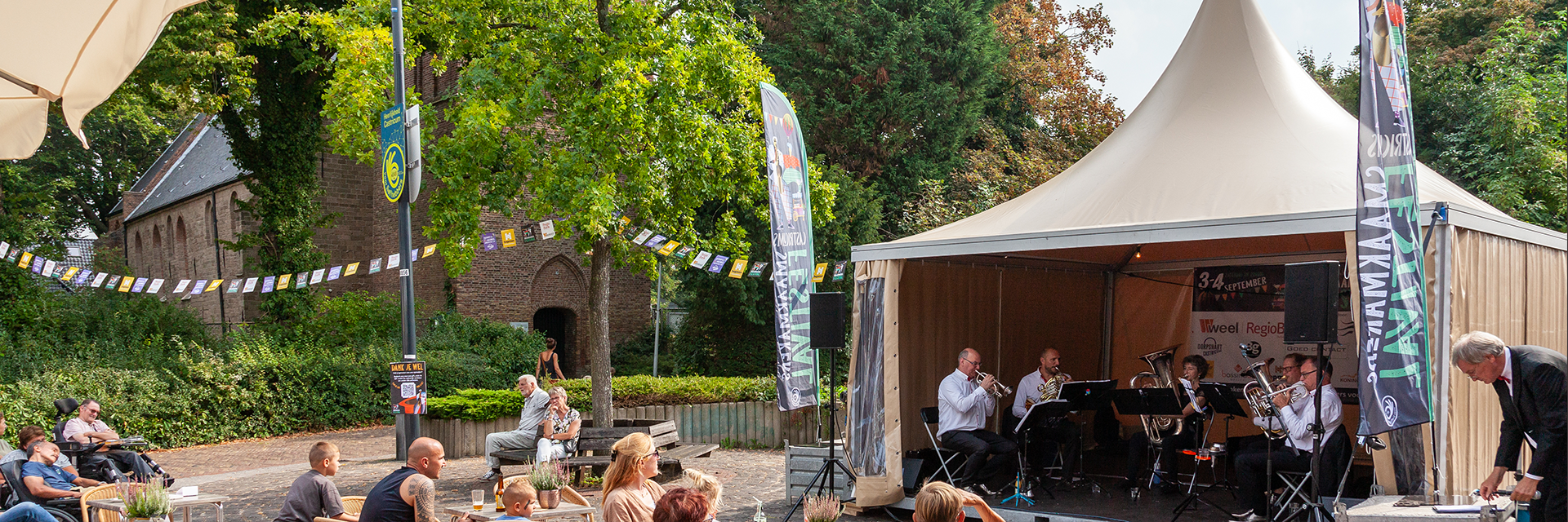 Kerk met muziektent ervoor en optreden van een orkest.