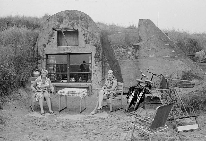 Historische foto van een bunker met twee personen er voor