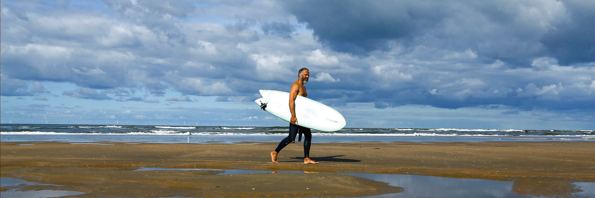 Man met surfplank onder zijn arm loopt naar de zee.